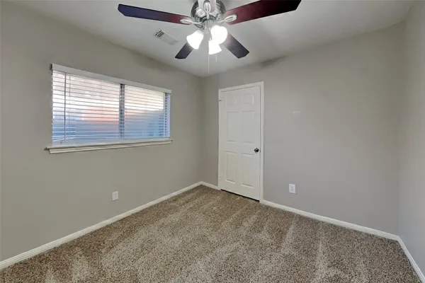 an empty room with chandelier fan and windows