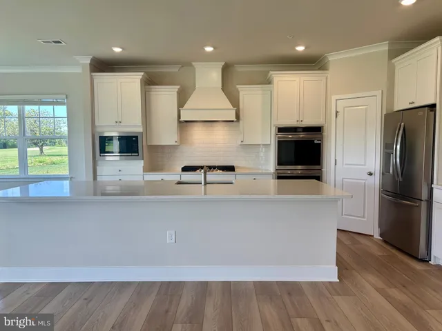 a large kitchen with stainless steel appliances a large counter top a stove a refrigerator with white cabinets and wooden floor