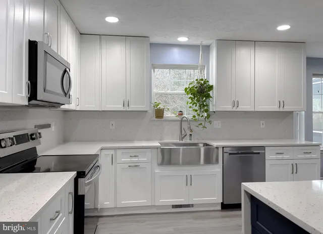 a kitchen with granite countertop a stove a sink a refrigerator and white cabinets with wooden floor