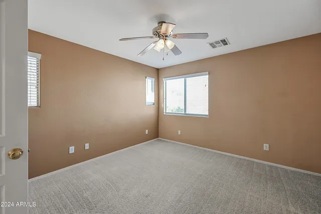 an empty room with a chandelier fan and windows
