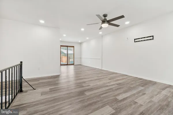 a view of an empty room with wooden floor and a ceiling fan