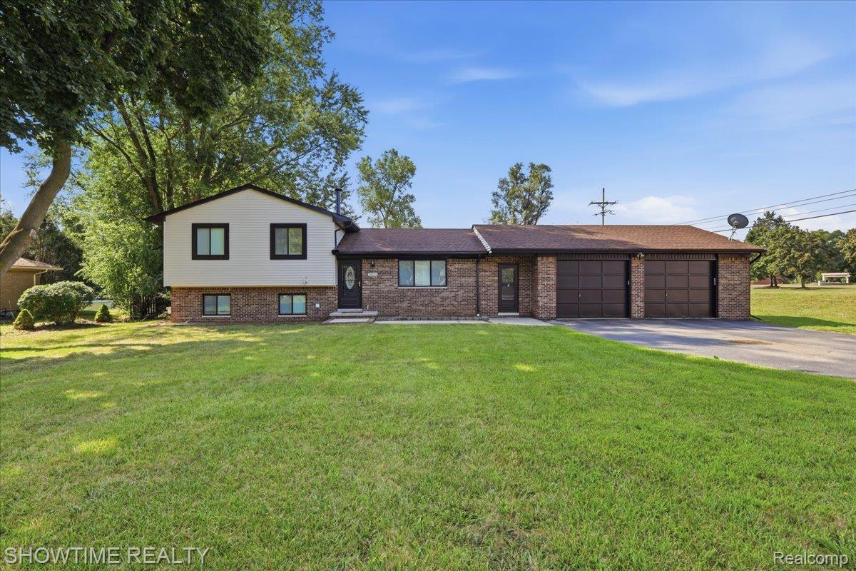 Brick and siding exterior with a pitched roof, featuring a two-car garage, a paved driveway, and a manicured lawn