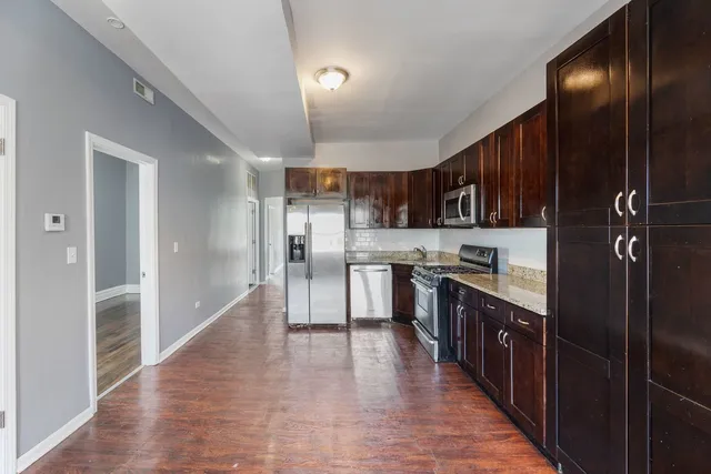 a kitchen with stainless steel appliances kitchen island granite countertop wooden floors wooden cabinets and sink