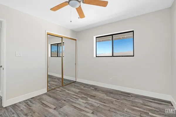 a view of an empty room with wooden floor and a ceiling fan