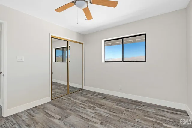 a view of an empty room with wooden floor and a ceiling fan