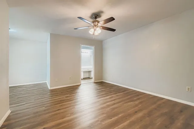 a view of an empty room with wooden floor and a ceiling fan