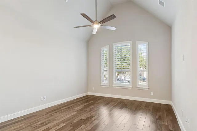 an empty room with wooden floor fan and windows