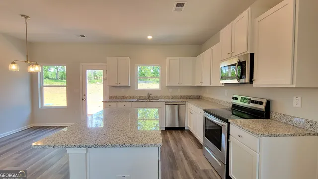 a kitchen with stainless steel appliances granite countertop a stove a sink and white cabinets with wooden floor