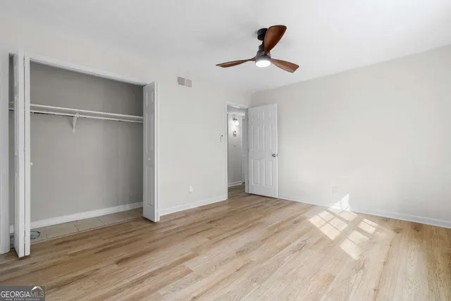 an empty room with wooden floor ceiling fan and windows