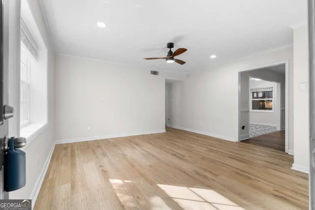 an empty room with wooden floor ceiling fan and windows