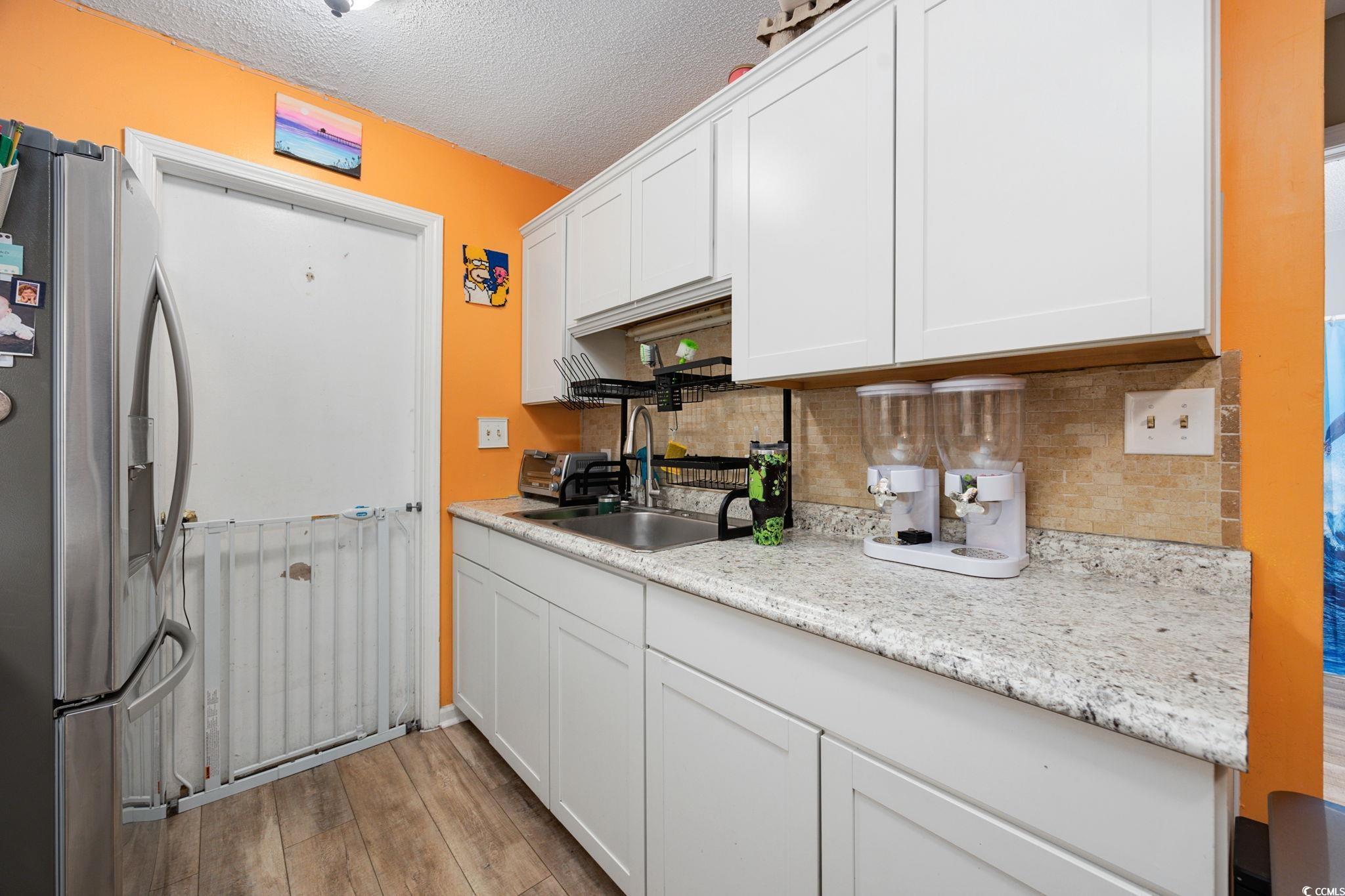 755 Burcale Road, Unit F4 Myrtle Beach, SC 29579 - Photo 10 of 30 Kitchen featuring stainless steel fridge with ice dispenser, a textured ceiling, tasteful backsplash, white cabinets, and light wood-style flooring