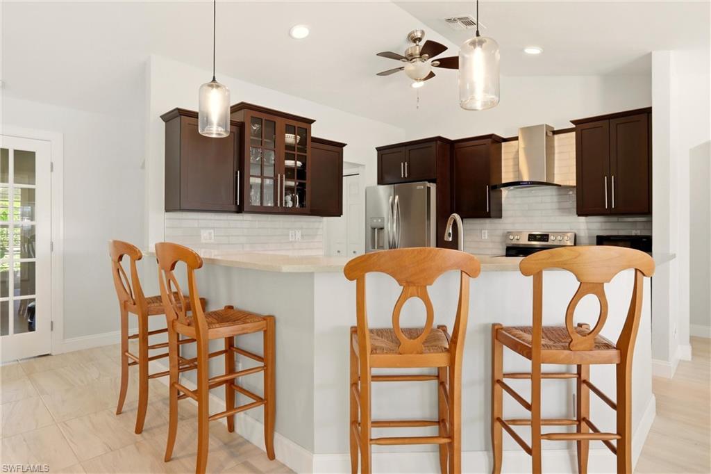 4282 Longshore Way North Naples, FL 34119 - Photo 9 of 43 Kitchen with dark wood finish cabinetry, a breakfast bar, decorative backsplash, and vaulted ceiling