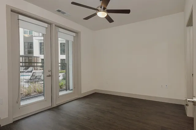 an empty room with wooden floor fan and windows