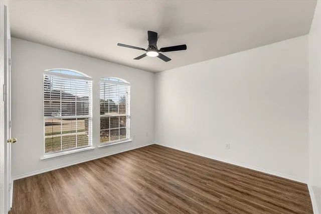 an empty room with wooden floor fan and windows