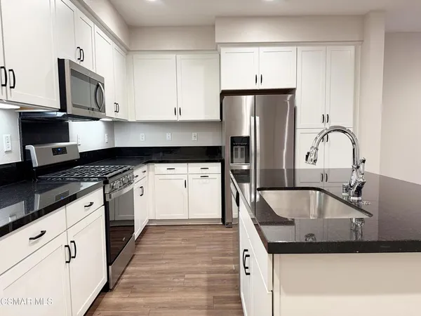 a kitchen with stainless steel appliances granite countertop a stove a sink and white cabinets