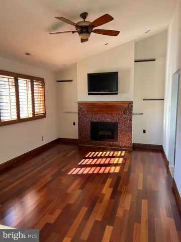 a view of an empty room with wooden floor fireplace and a window