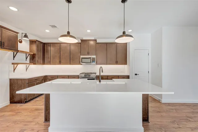 a large kitchen with kitchen island a sink a stove a refrigerator and a dining table with wooden floor