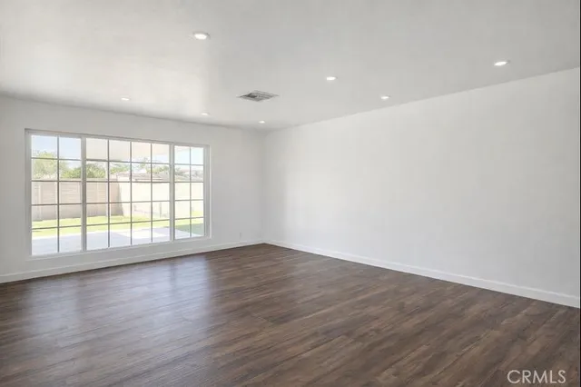 an empty room with wooden floor and windows with curtains