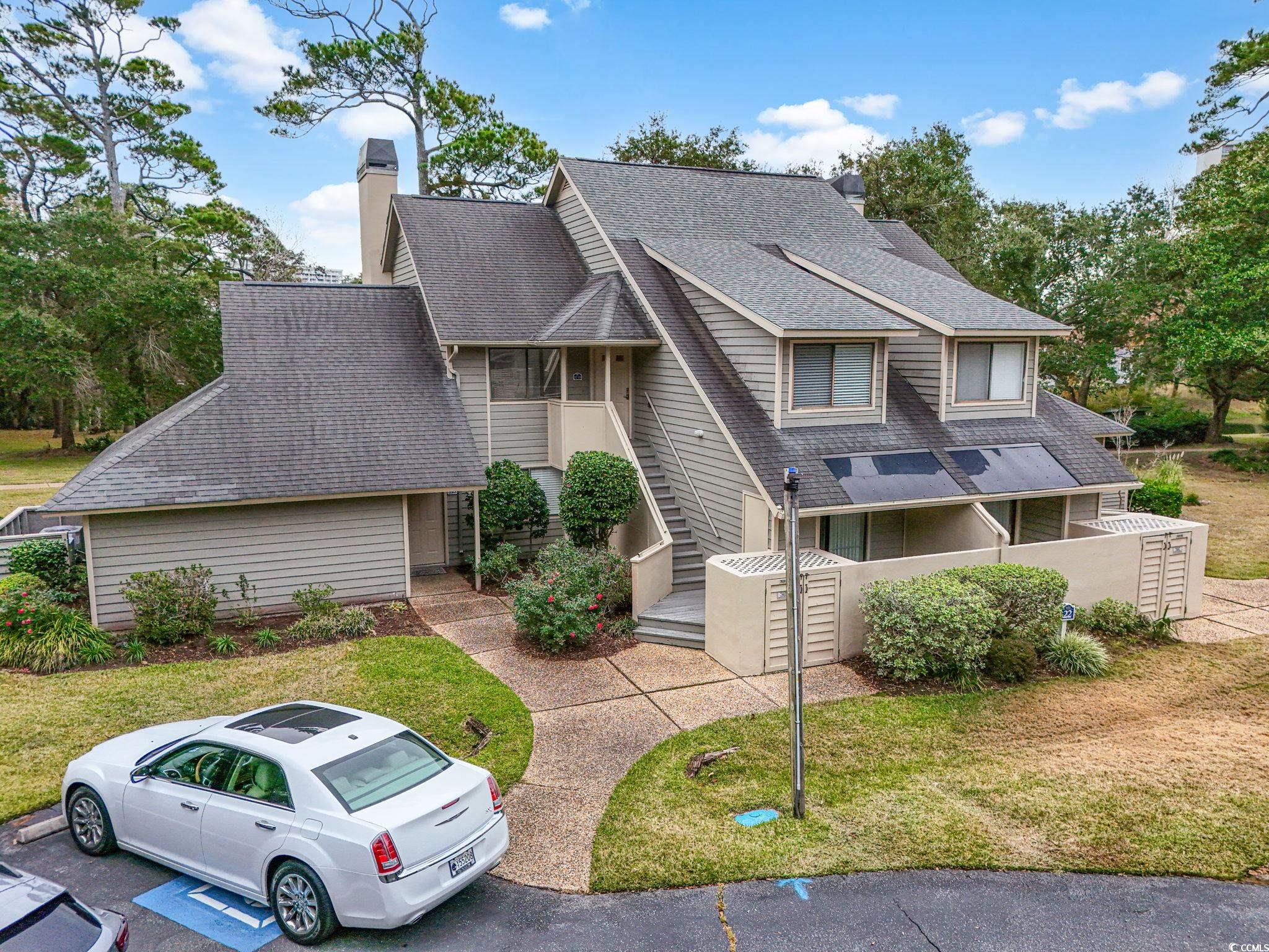 Mid-century modern home with a shingled roof, a chimney, a front yard, and a balcony