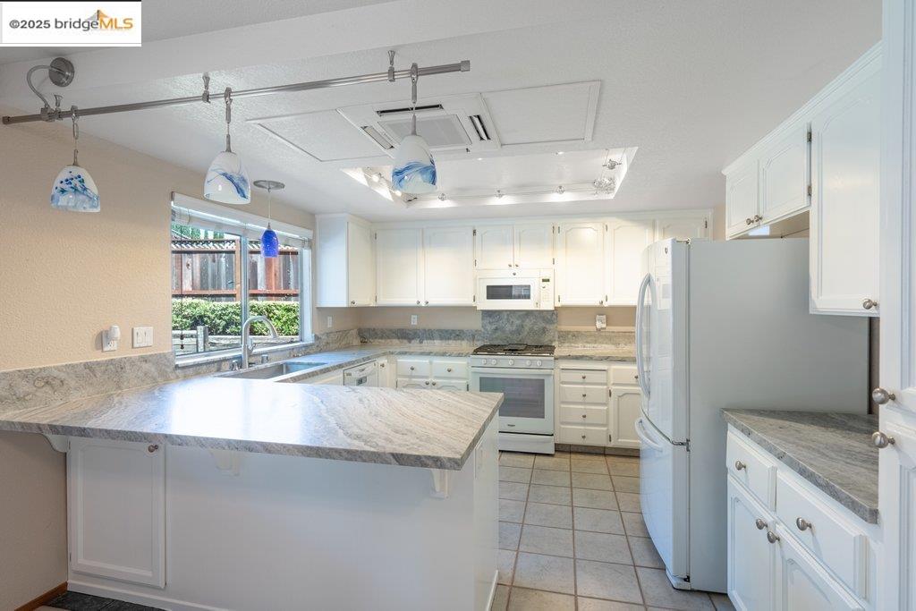 1003 Linda Vista Way Rio Vista, CA 94571 - Photo 17 of 60 Kitchen with a peninsula, white appliances, white cabinetry, light tile patterned floors, and light stone counters