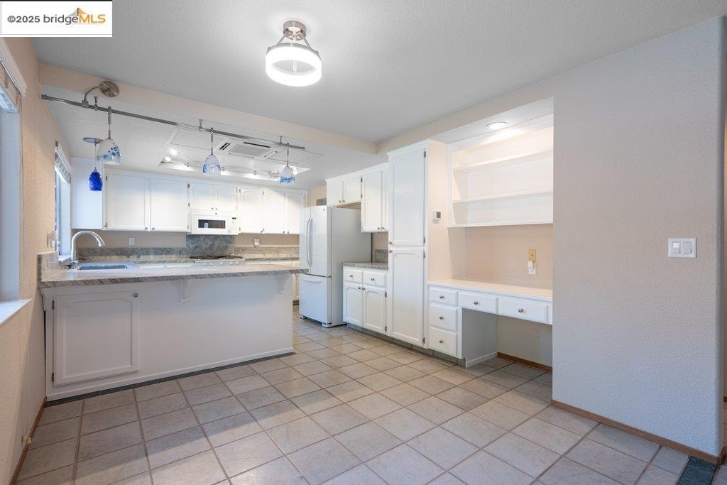 1003 Linda Vista Way Rio Vista, CA 94571 - Photo 19 of 60 Kitchen featuring a peninsula, built in desk, white cabinetry, open shelves, and white appliances