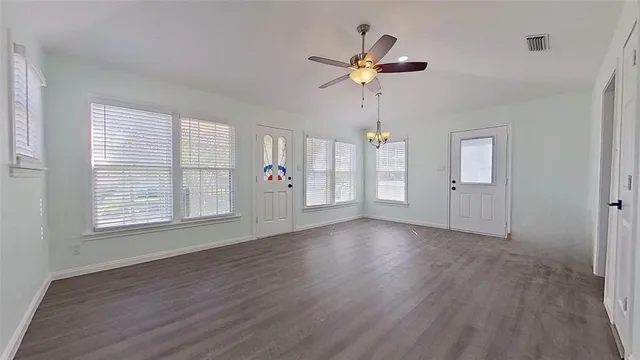 an empty room with wooden floor chandelier fan and windows