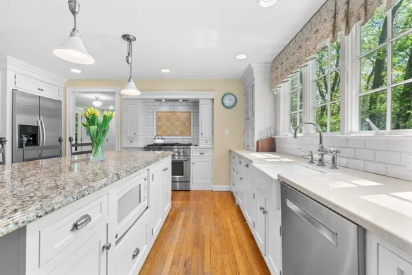a large kitchen with granite countertop a sink dishwasher a stove and white cabinets with wooden floor