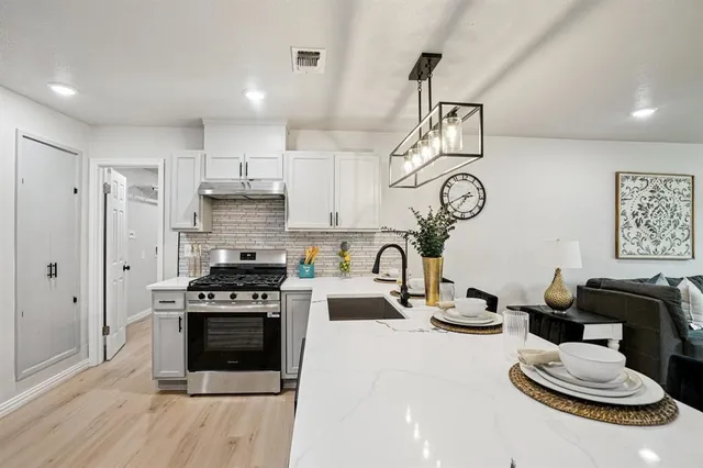 a kitchen with stainless steel appliances granite countertop a sink dishwasher stove and white cabinets with wooden floor