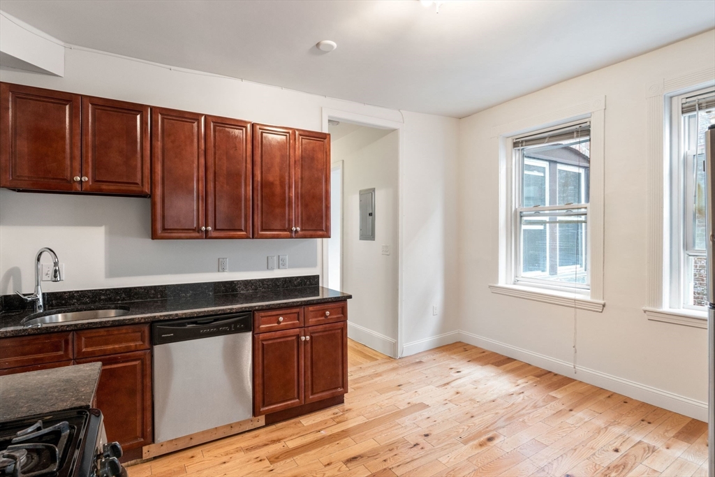 80-84 Shepton Street, Unit 803 Boston, MA 02124 - Photo 4 of 16 a kitchen with granite countertop wooden cabinets a stove a sink and a window