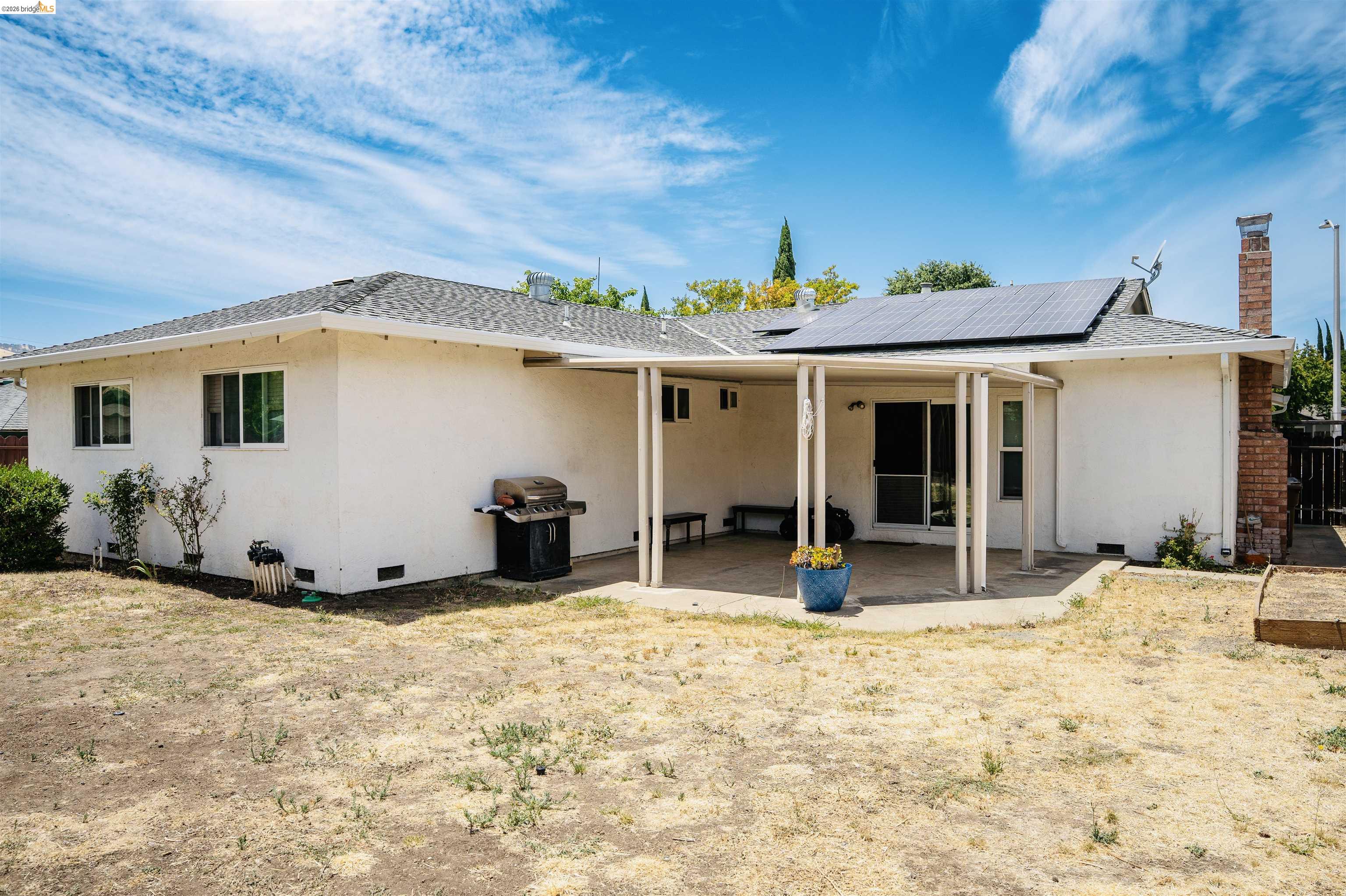 3513 Rio Grande Drive Antioch, CA 94509 - Photo 20 of 22 Rear exterior featuring a covered patio, multiple windows, a shingle roof, solar panel installation, and a brick chimney