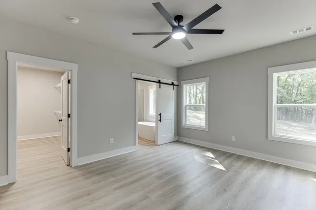 a view of an empty room with wooden floor a ceiling fan and windows