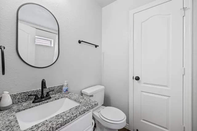 a bathroom with a granite countertop toilet a sink and a mirror