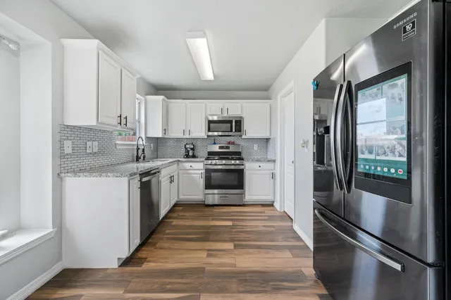 a kitchen with granite countertop a refrigerator a sink and white cabinets