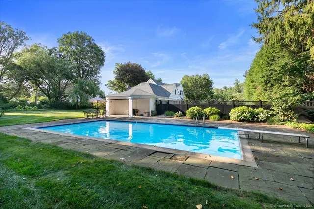 a view of pool with lawn chairs and large trees
