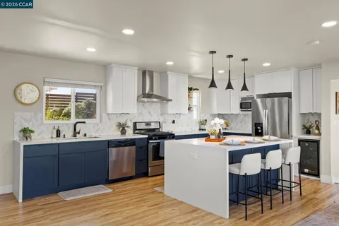 a kitchen with stainless steel appliances kitchen island granite countertop a sink a stove a refrigerator and a dining table with wooden floor