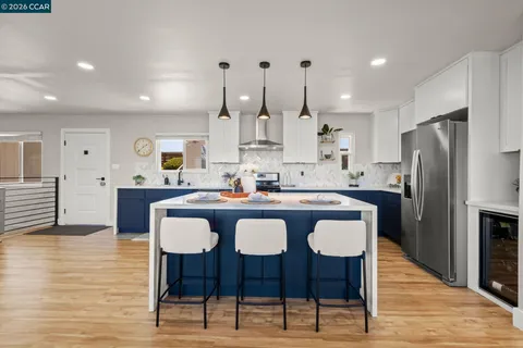 a kitchen with stainless steel appliances kitchen island granite countertop a dining table chairs and a refrigerator