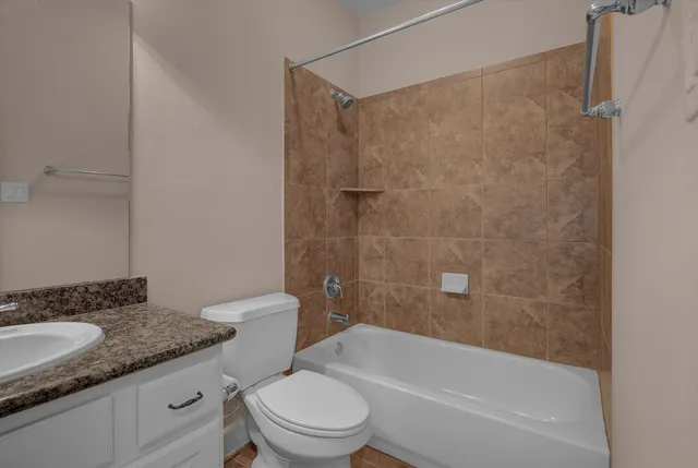 a bathroom with a granite countertop bathtub shower sink vanity and toilet