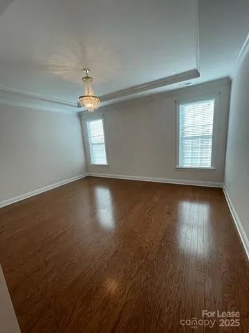 an empty room with wooden floor chandelier and windows