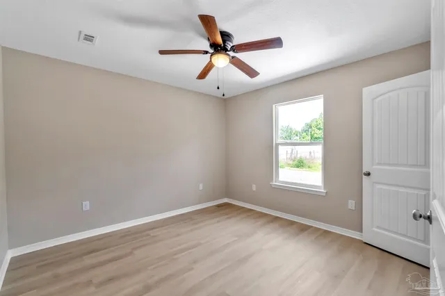 an empty room with wooden floor ceiling fan and windows