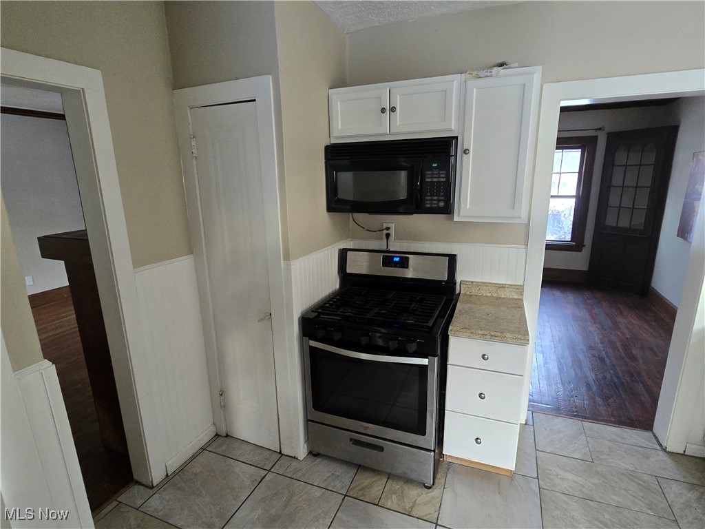 2048 Rossmoor Road Cleveland Heights, OH 44118 - Photo 9 of 29 Kitchen with stainless steel range with gas stovetop, white cabinets, light countertops, black microwave, and a wainscoted wall