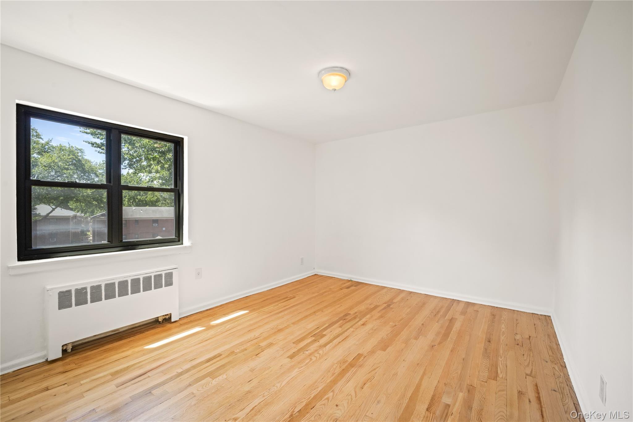 73-10 Springfield Boulevard, Unit B Queens, NY 11364 - Photo 10 of 20 Spare room featuring radiator and light wood-style floors