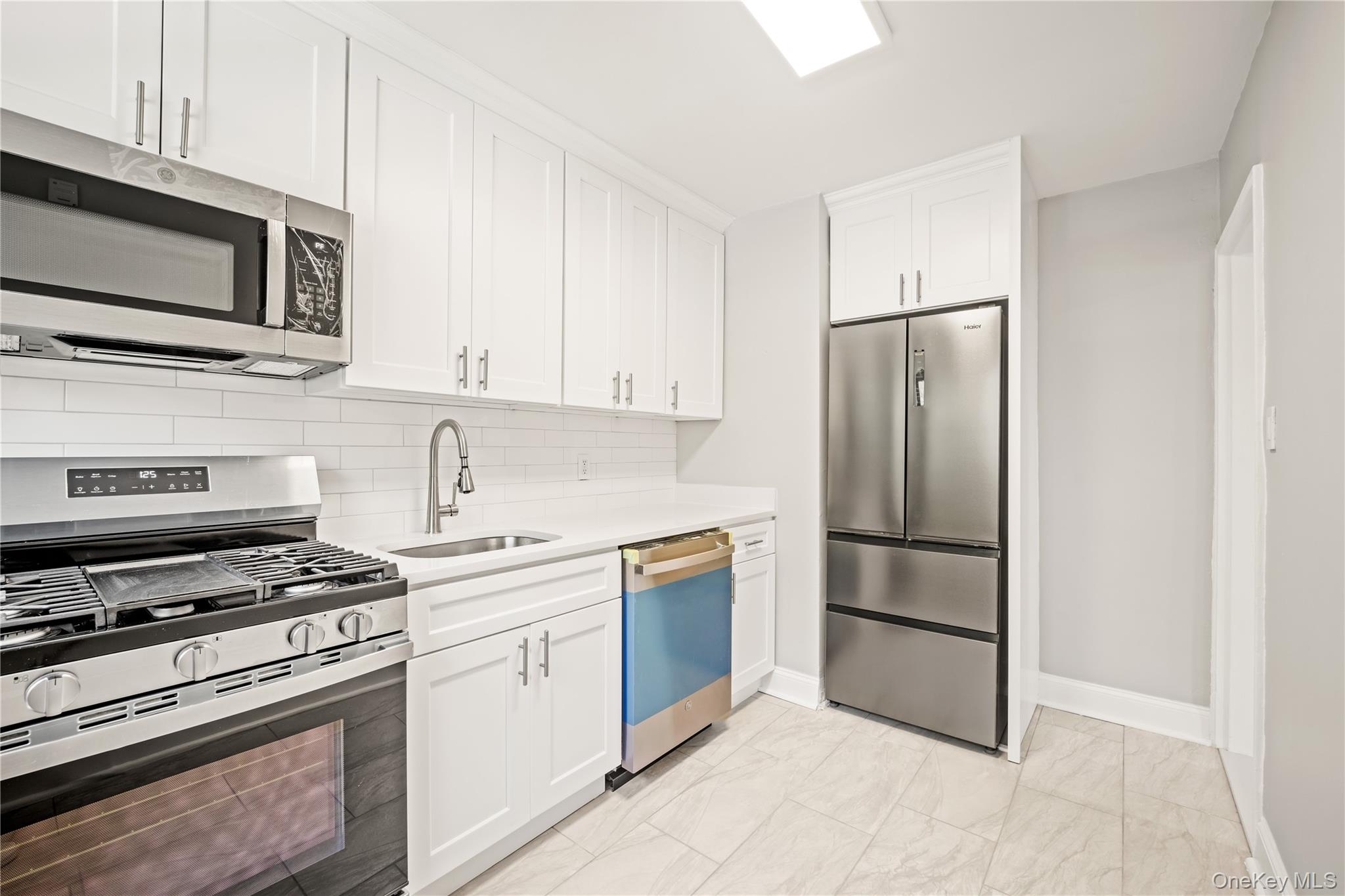 73-10 Springfield Boulevard, Unit B Queens, NY 11364 - Photo 12 of 20 Kitchen with stainless steel appliances, white cabinetry, light stone countertops, and tasteful backsplash