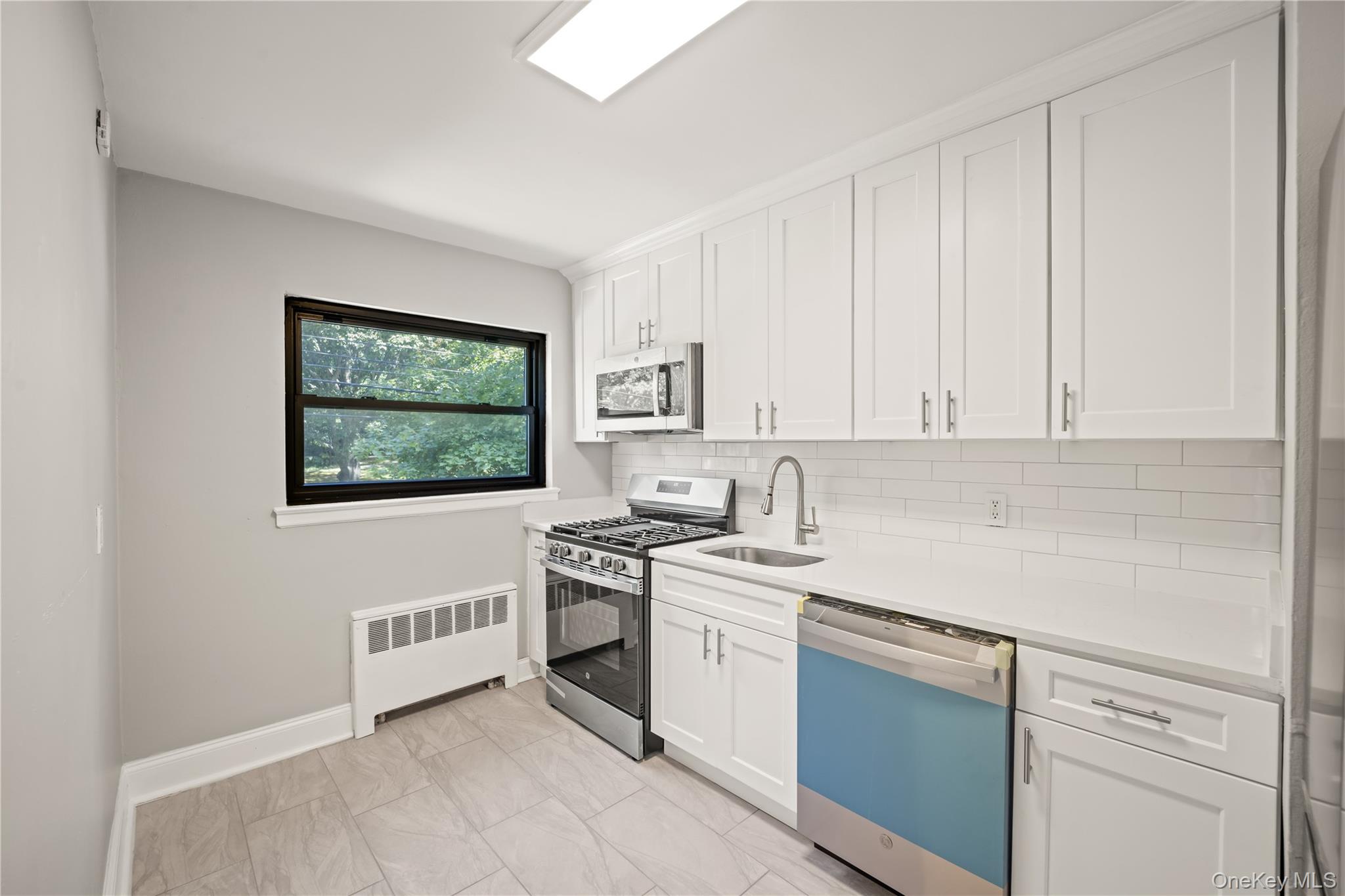 73-10 Springfield Boulevard, Unit B Queens, NY 11364 - Photo 13 of 20 Kitchen featuring stainless steel appliances, radiator, decorative backsplash, and white cabinets