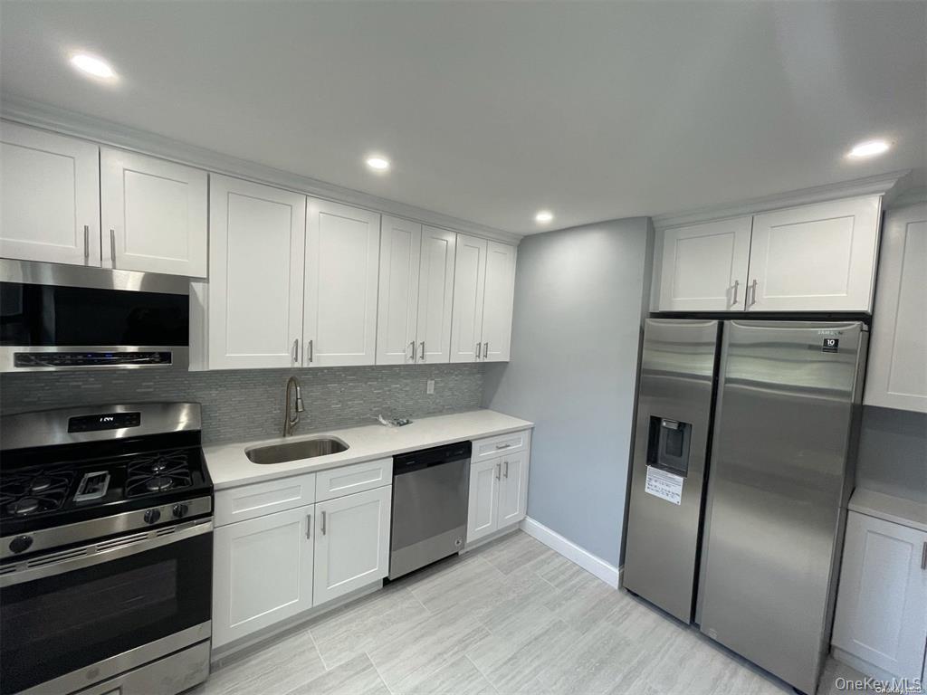 73-10 Springfield Boulevard, Unit B Queens, NY 11364 - Photo 15 of 20 Kitchen featuring stainless steel appliances, backsplash, white cabinetry, light countertops, and recessed lighting