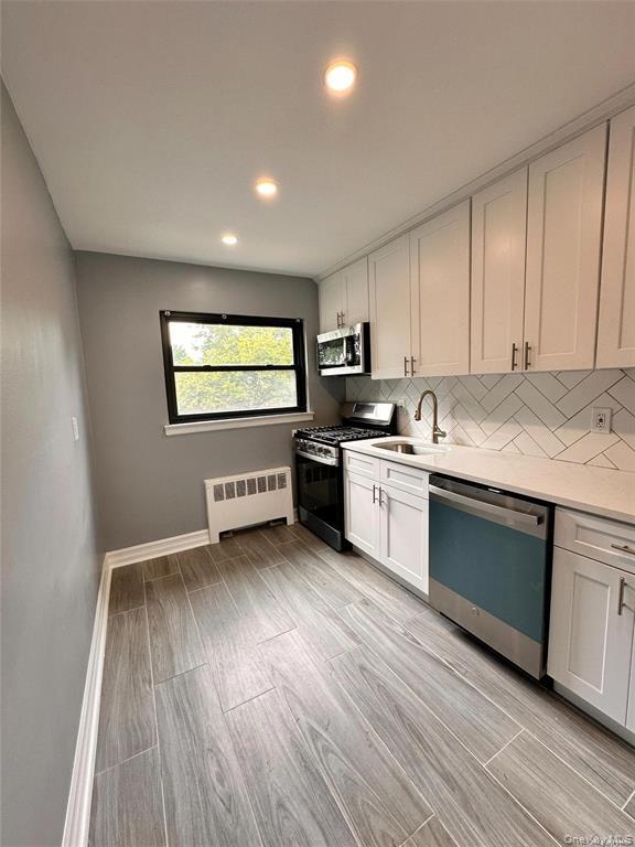 73-10 Springfield Boulevard, Unit B Queens, NY 11364 - Photo 16 of 20 Kitchen featuring stainless steel appliances, tasteful backsplash, recessed lighting, radiator heating unit, and light wood-style flooring