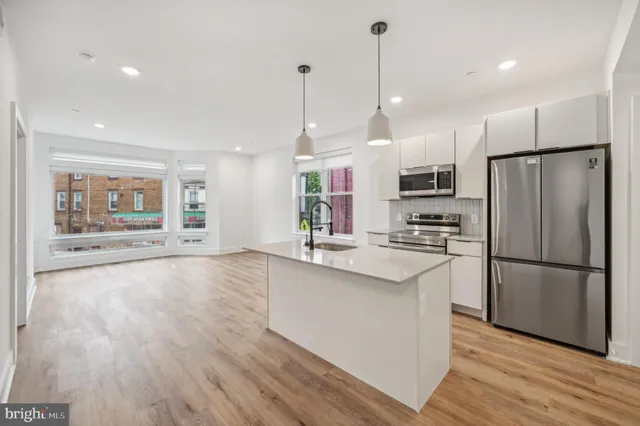 a open kitchen with stainless steel appliances granite countertop a refrigerator a sink dishwasher a stove and white cabinets with wooden floor