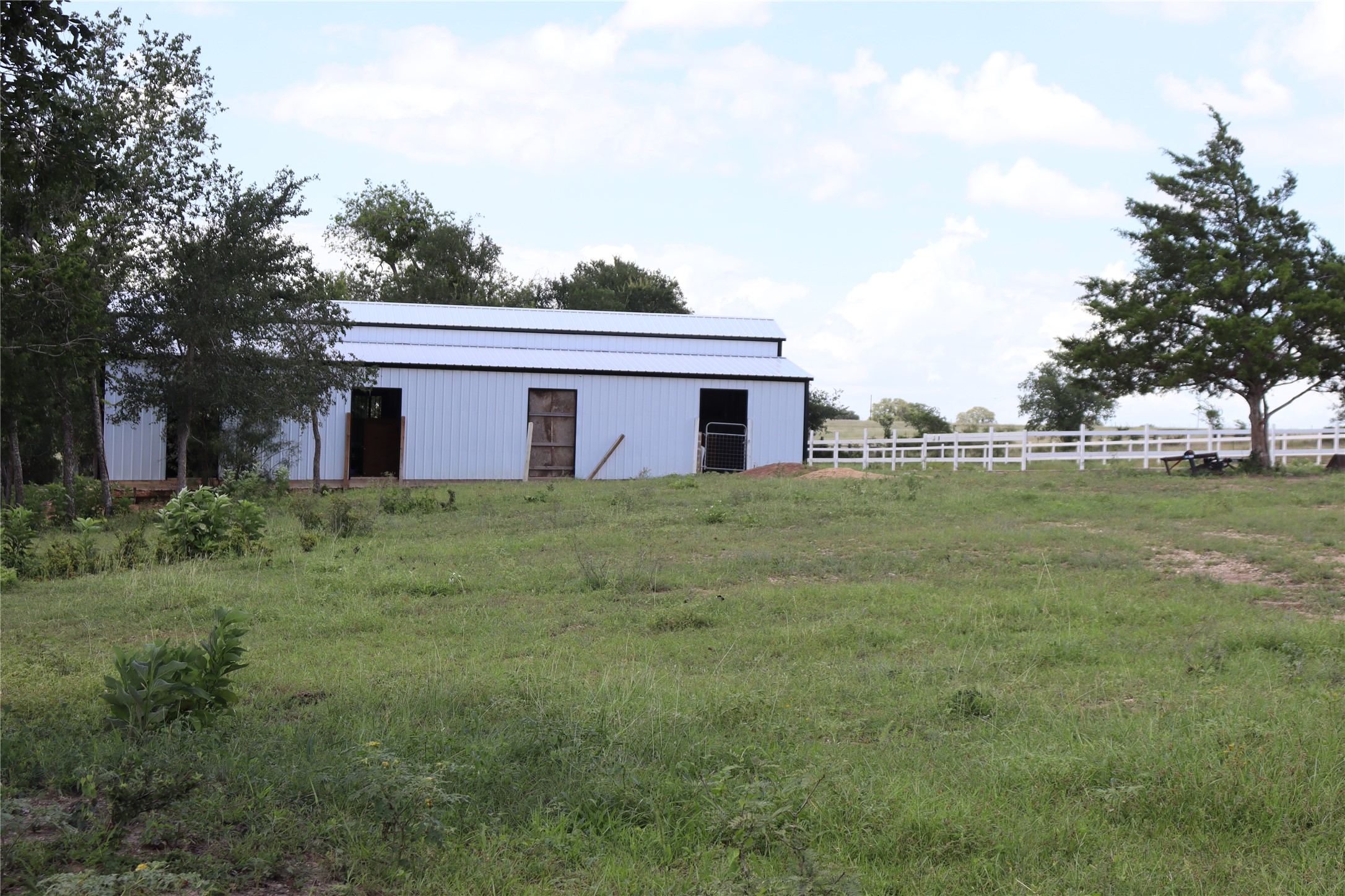 1220 Brushy Branch Road Lockhart, TX 78644 - Photo 9 of 14 A spacious pasture with a clean barn and a charming white fence, perfect for animals and outdoor living.
