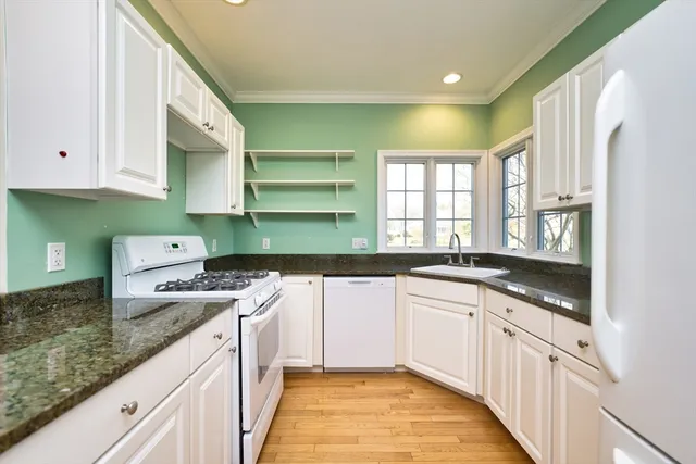 a kitchen with granite countertop a sink stainless steel appliances white cabinets and a window