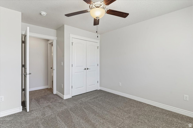 2028 West Grace Way Layton, UT 84041 - Photo 20 of 36 Unfurnished bedroom featuring a textured ceiling, dark colored carpet, a closet, and a ceiling fan