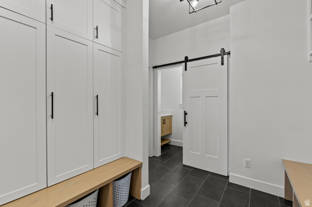 3111 South 1250 West Logan, UT 84321 - Photo 13 of 51 White shaker-style cabinetry with black hardware, natural wood-finish bench, dark tile flooring, and a sliding barn door with black track